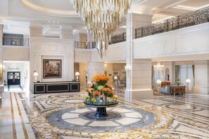 A grand lobby with a central floral arrangement, a staircase, and a reception desk. - The Plaza Doha, LXR Hotels & Resorts (Doha)