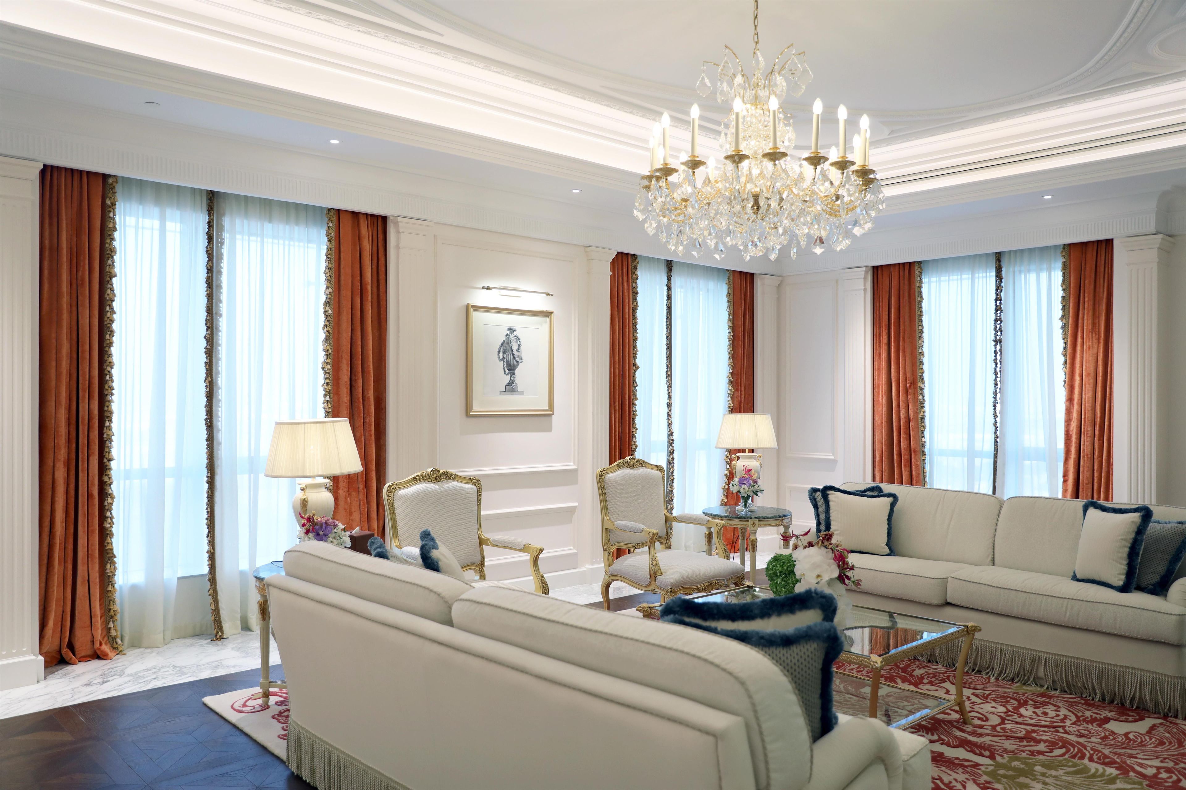 A luxurious living room with a chandelier, elegant furniture, and a large window with curtains.