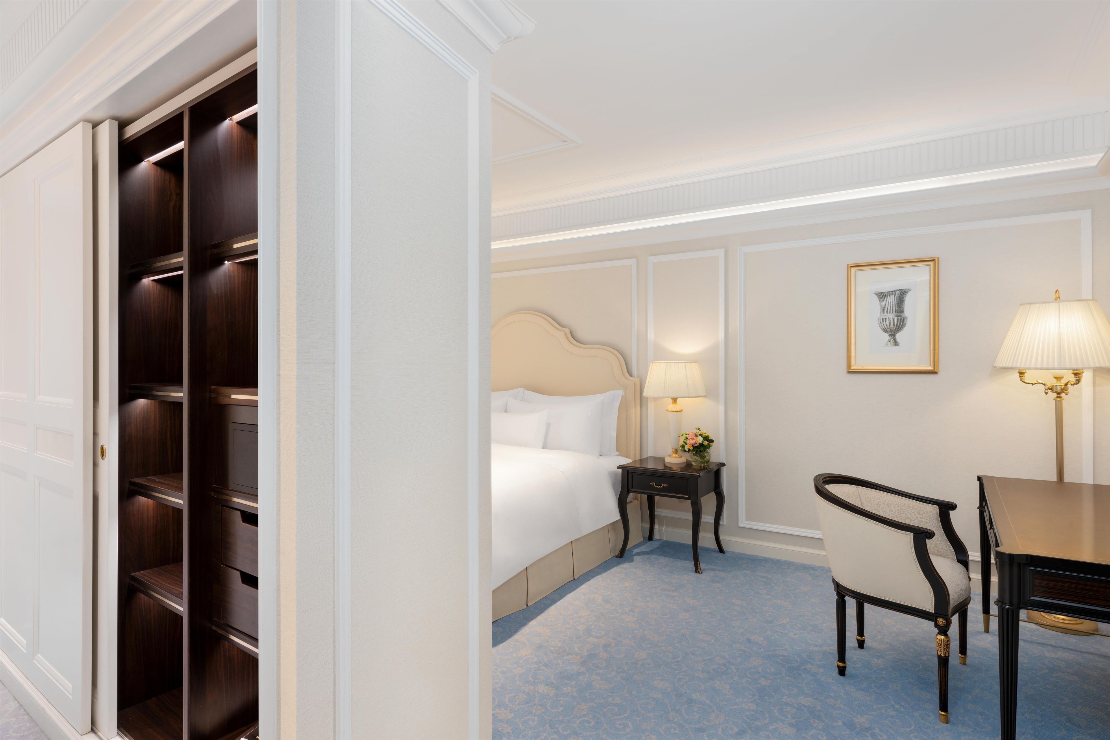 A hotel room with a bed, bedside table, lamp, chair, and a wardrobe.