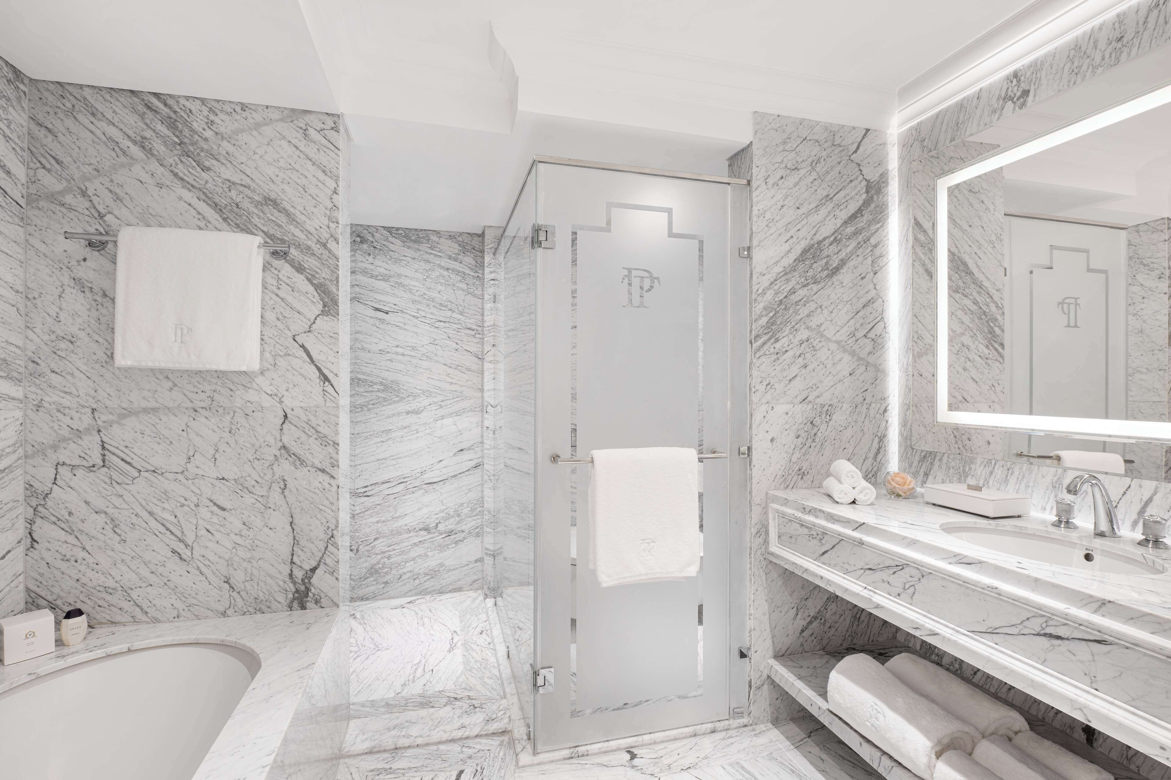 Une salle de bain moderne avec un sol en marbre, une douche en verre, un grand miroir et une baignoire blanche.