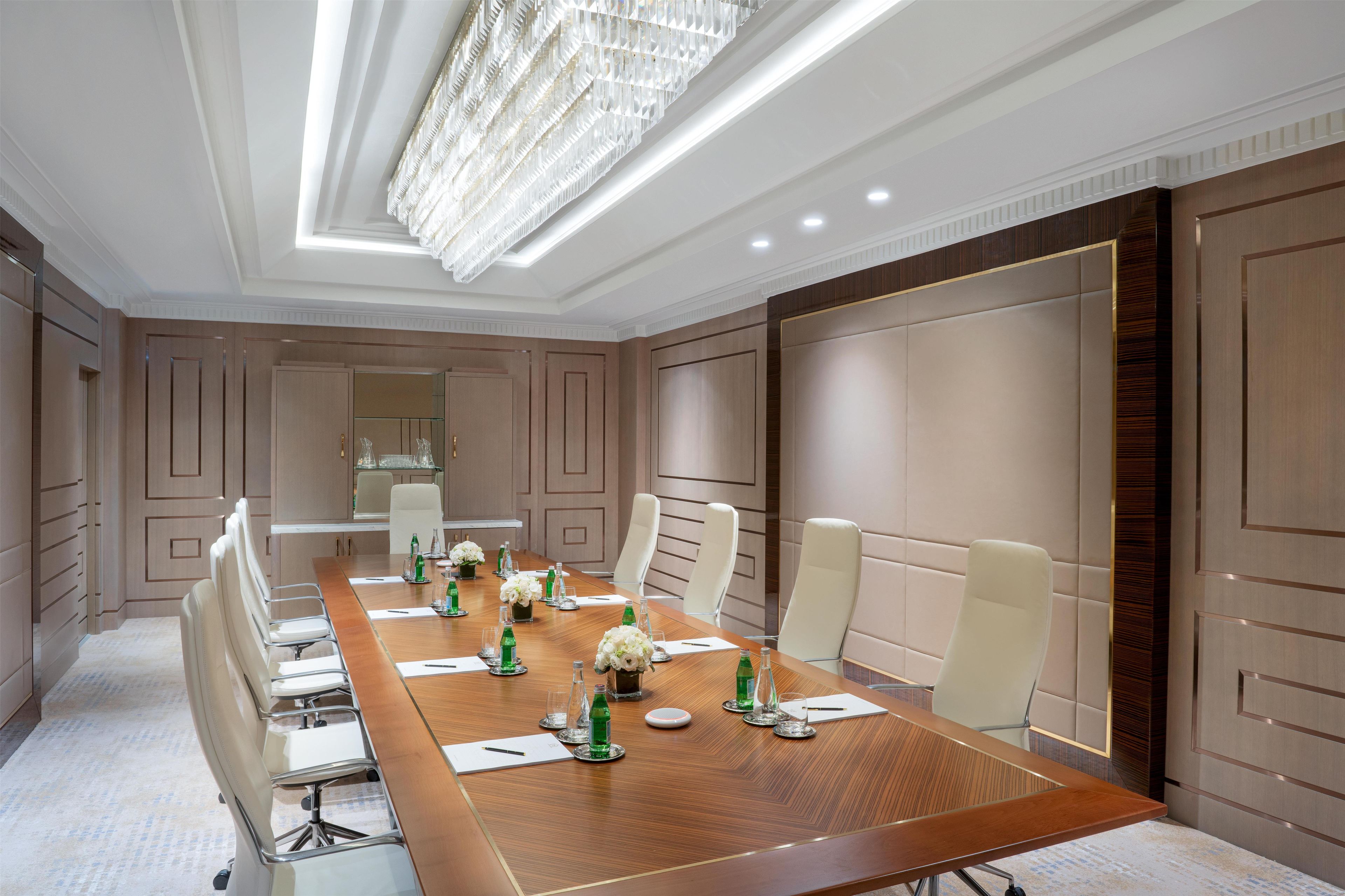 A conference room with a long table, white chairs, and a chandelier.