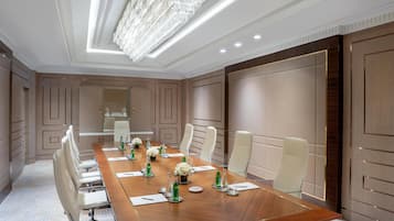 A conference room with a long table, white chairs, and a chandelier.
