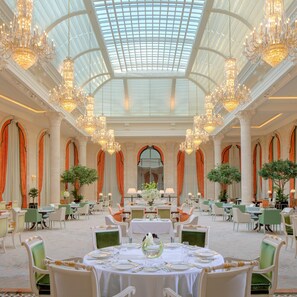 A grand dining hall with high ceilings, ornate chandeliers, and a glass dome. Tables are set with fine china and green upholstered chairs. - The Plaza Doha, LXR Hotels & Resorts (Doha)