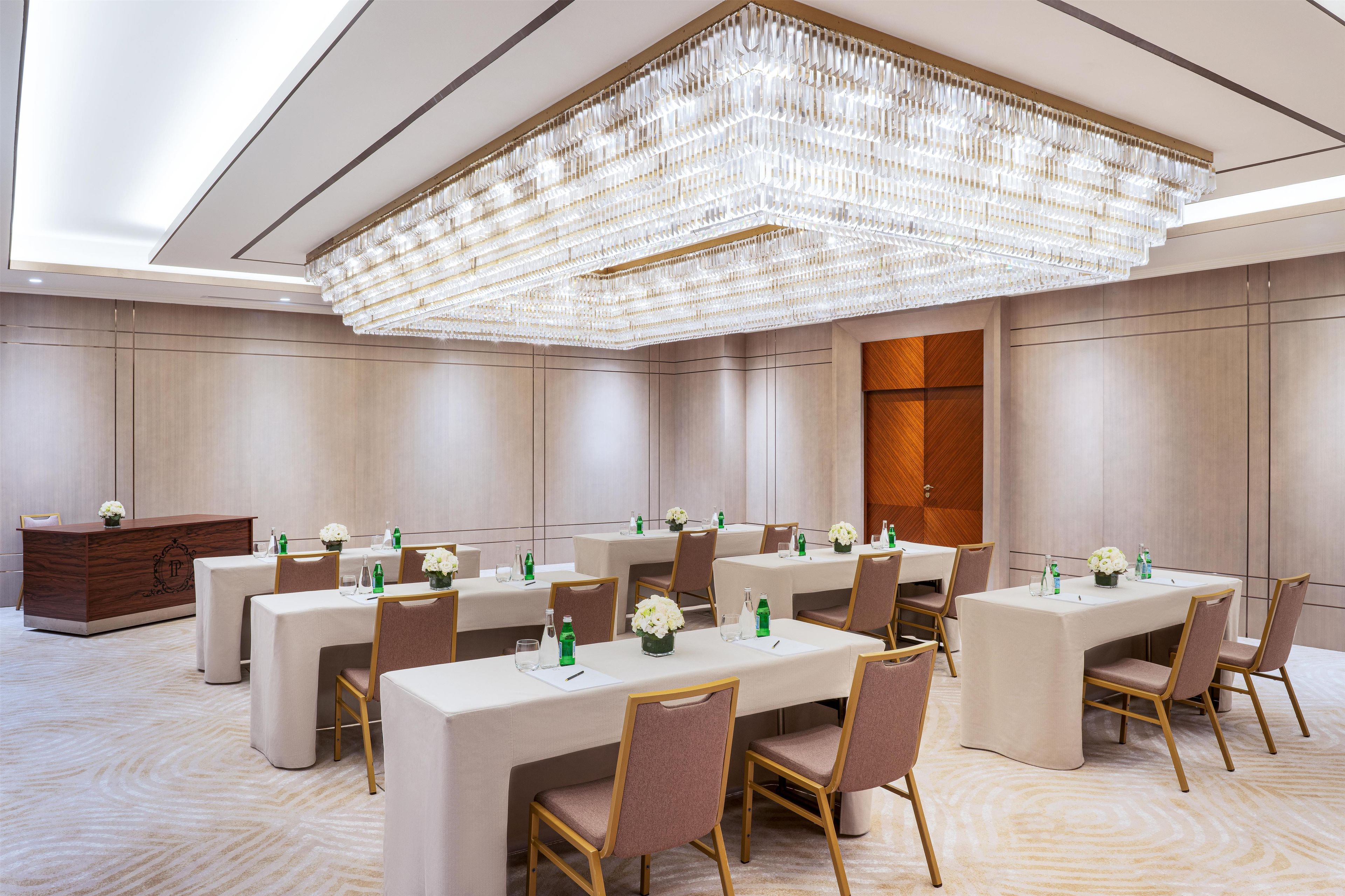 A conference room with a large chandelier, multiple tables with chairs, and a reception desk.