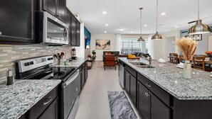 A modern kitchen with dark cabinetry, stainless steel appliances, and granite countertops. - Luxury 8BR Villa Near Disney | Private Pool & Spa | Windsor Island Resort (Davenport)