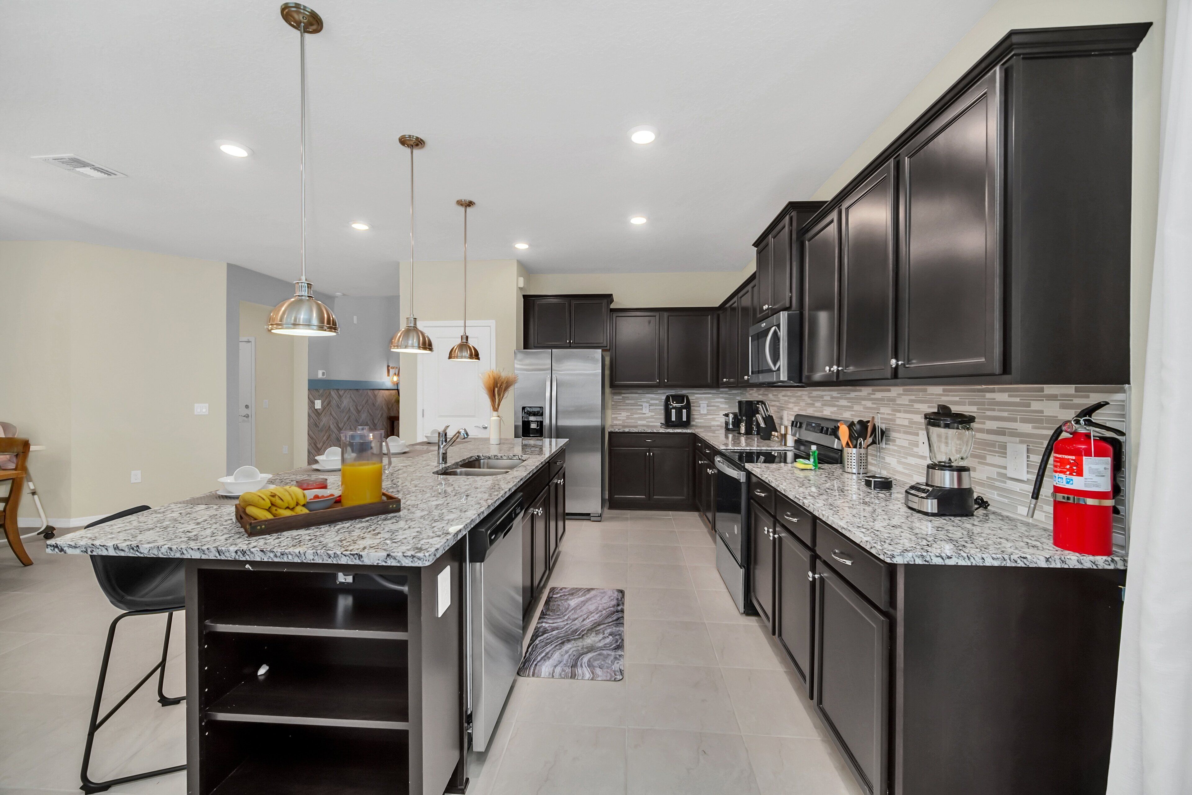 A modern kitchen with dark cabinets, stainless steel appliances, and a marble countertop.