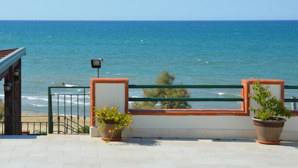 Un balcon donnant sur la mer, une balustrade et deux plantes en pot.