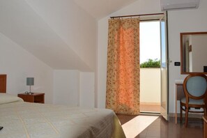 Un dormitori amb un llit, una tauleta de nit, una cadira, un escriptori i una finestra amb cortines.