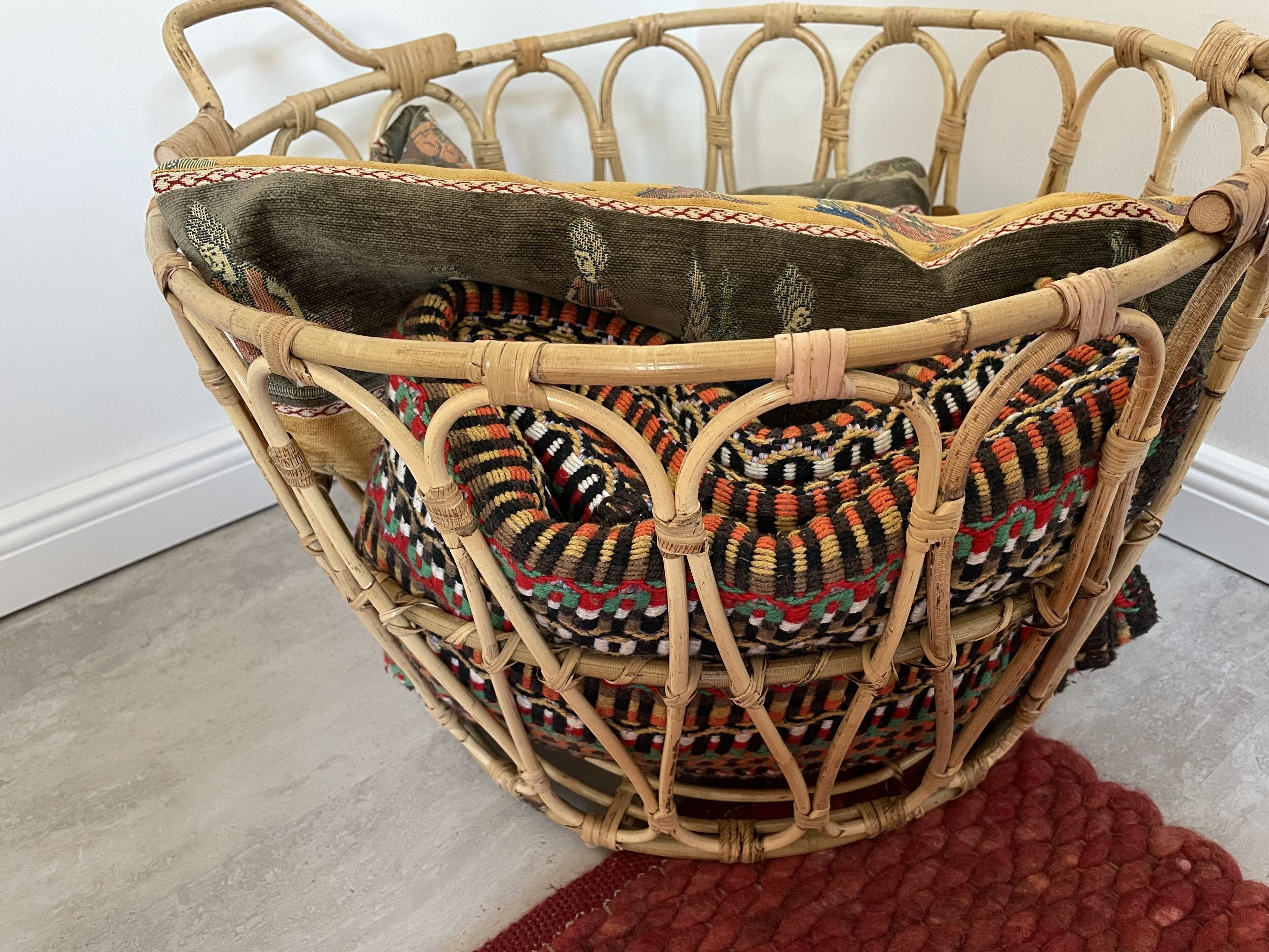 A wicker chair with a woven seat and backrest, placed on a red rug.