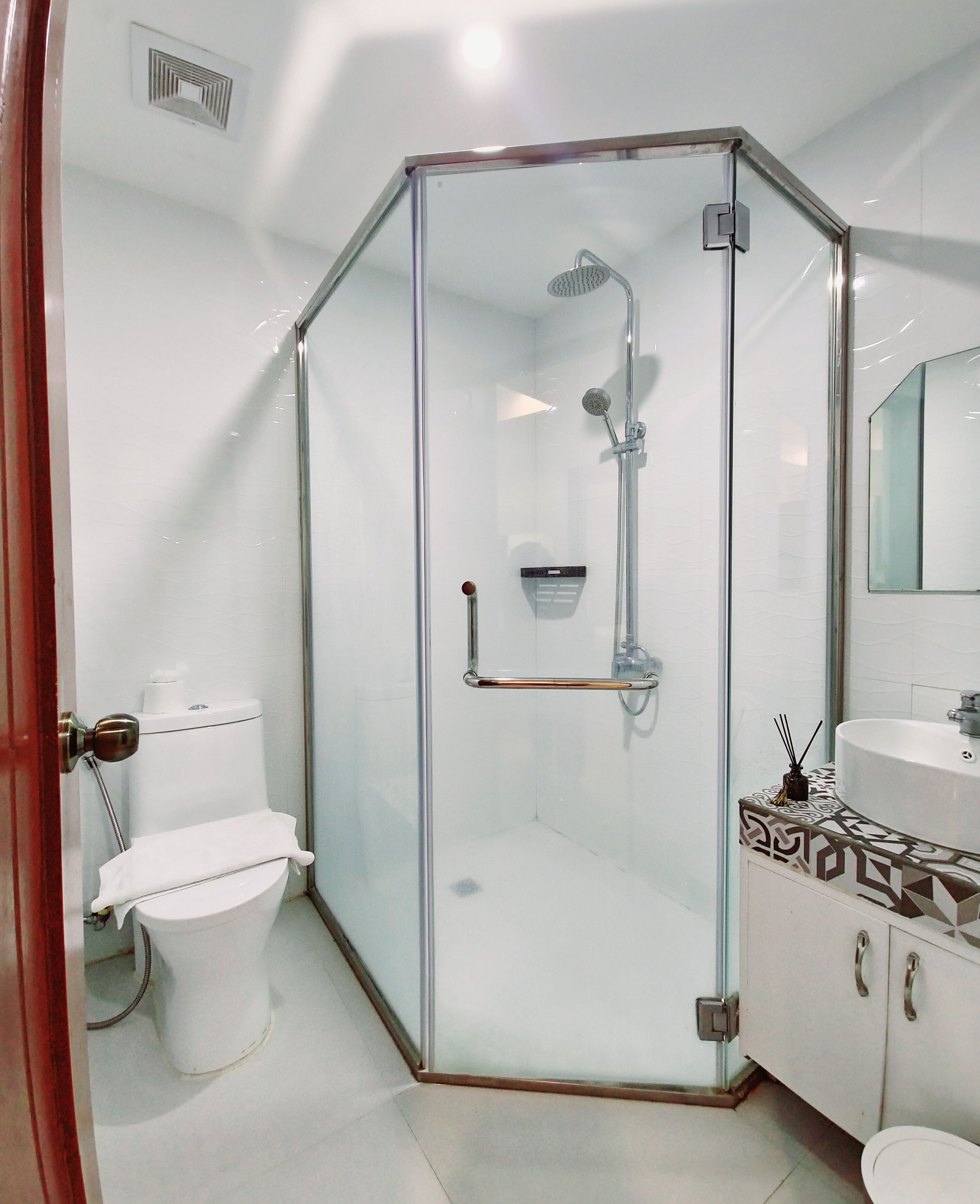 A modern bathroom with a glass-enclosed shower, a toilet, and a sink with a mirror.