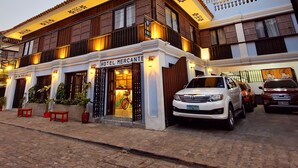 A hotel with a traditional facade, a gated entrance, and a parking area with cars. - Hotel Mercante (Vigan)