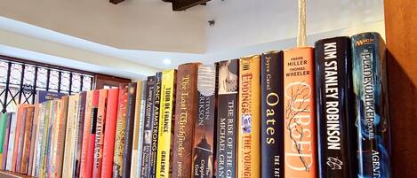 Une bibliothèque remplie de divers ouvrages, placée sous un plafond en bois avec des poutres apparentes et des lampes suspendues.