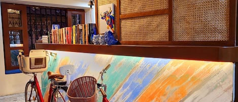 A red bicycle parked in front of a colorful mural, a bookshelf with books, and a decorative wall panel.