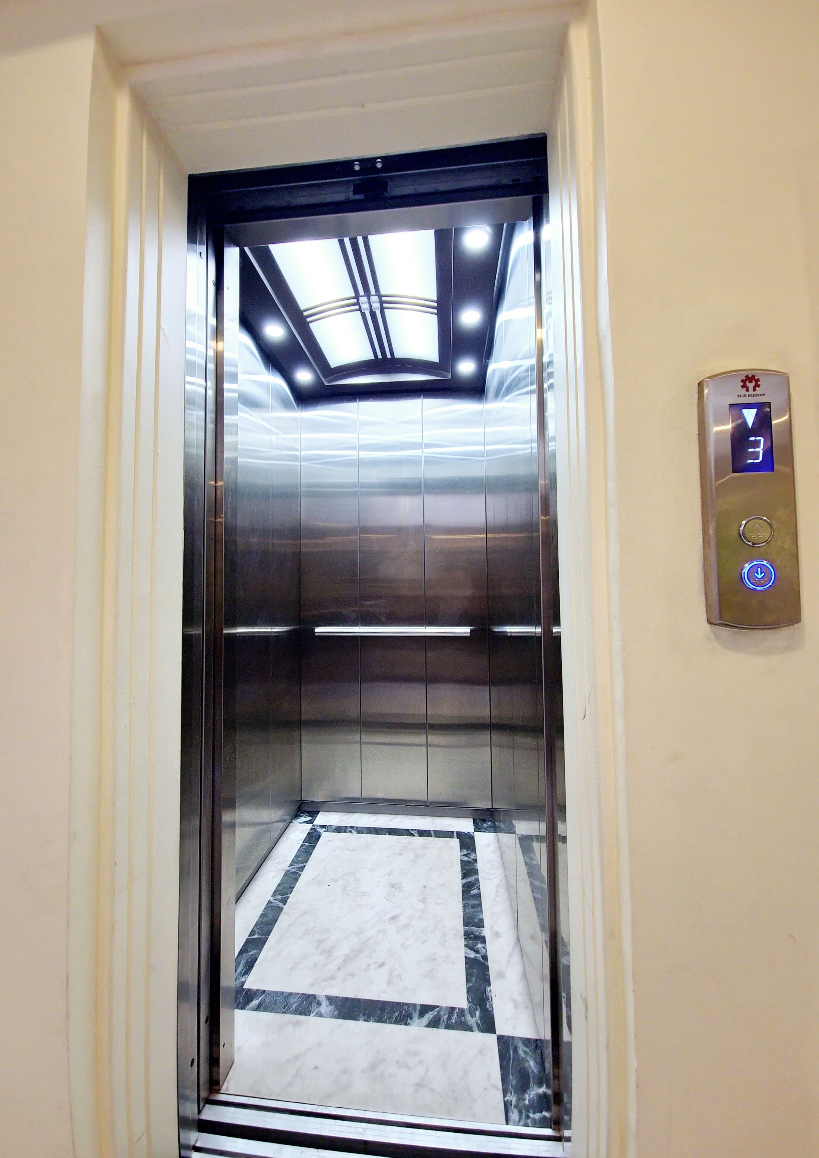 Un ascensor con pantalla digital, suelo de mármol e iluminación empotrada en el techo.
