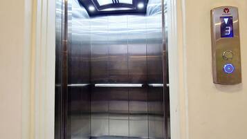 Un ascensor con pantalla digital, suelo de mármol e iluminación empotrada en el techo.