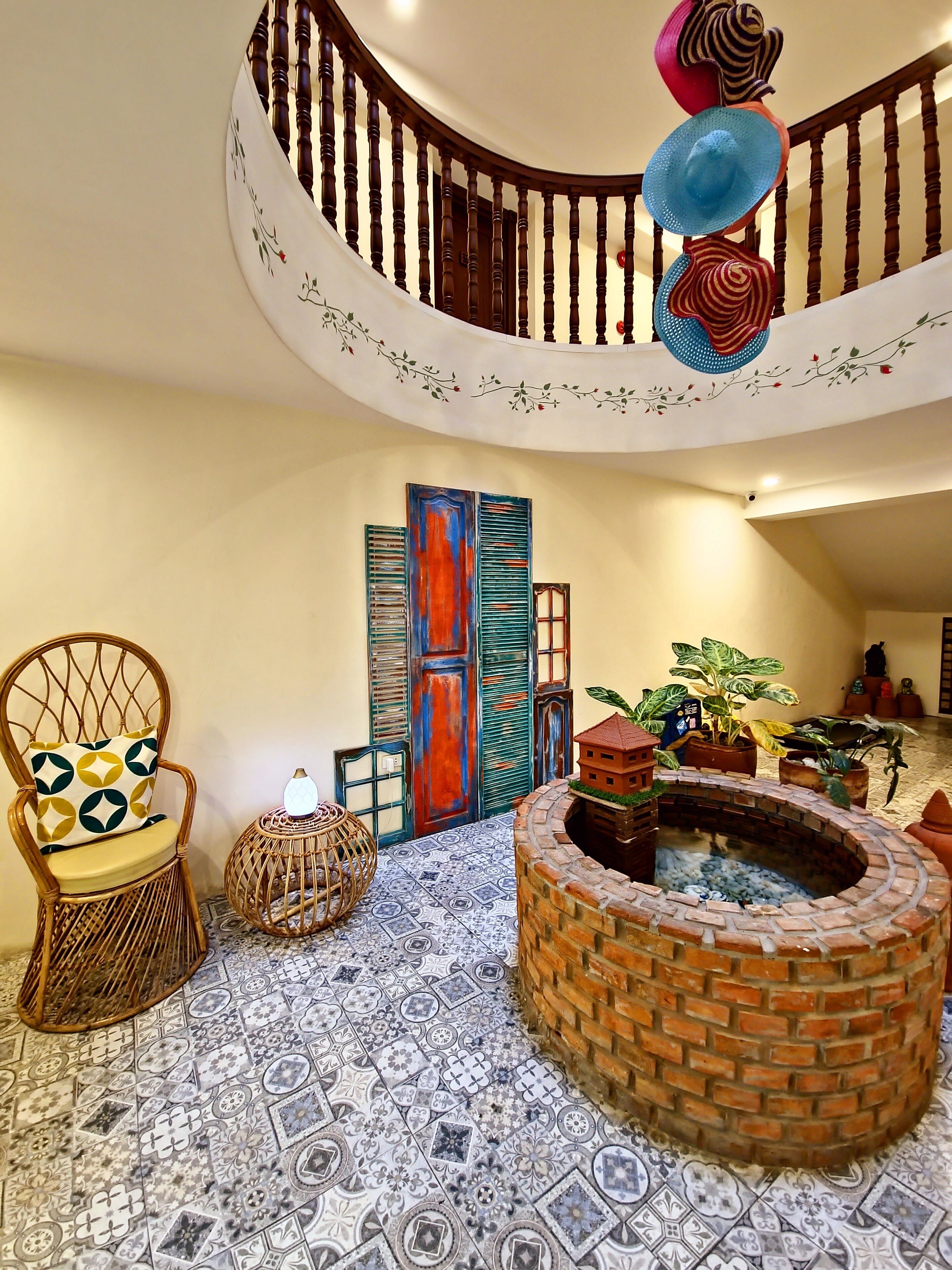 A spacious interior with a curved wooden staircase, a decorative fireplace, patterned floor tiles, and a wicker chair with a patterned cushion.