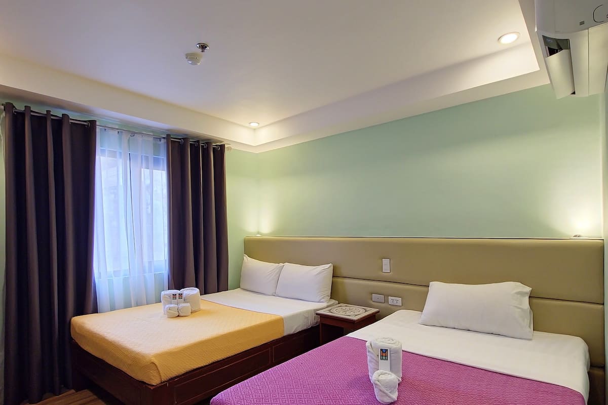 A hotel room with two beds, a wooden floor, and an air conditioning unit on the wall.