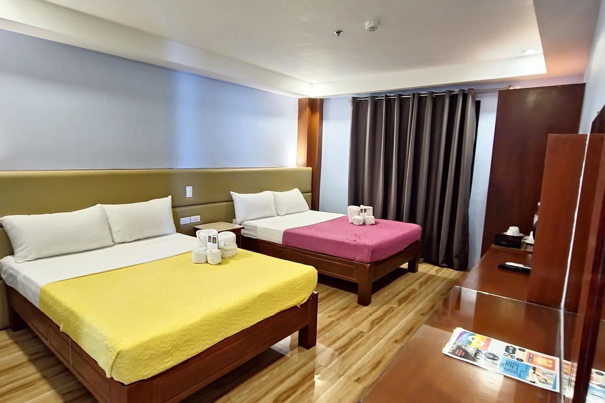 A hotel room with two beds, a wooden floor, a desk with a magazine, and a large window with curtains.