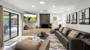 Una sala de estar moderna con un televisor de pantalla plana grande, una chimenea y una piscina visible a través de puertas de vidrio.
