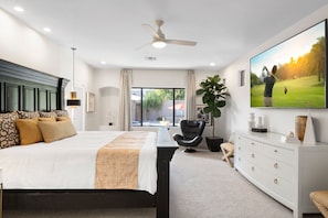 A modern bedroom with a large bed, a ceiling fan, a TV, a desk, and a view of a golf course.