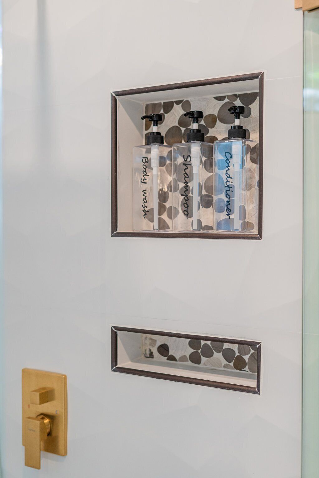 Un baño con pared blanca, picaporte dorado y tres botellas de jabón, champú y acondicionador en un expositor decorativo.