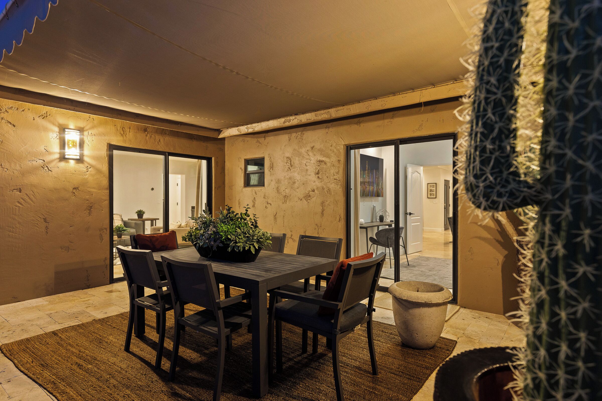 An outdoor patio with a wooden table and chairs, a potted plant, and a concrete planter.