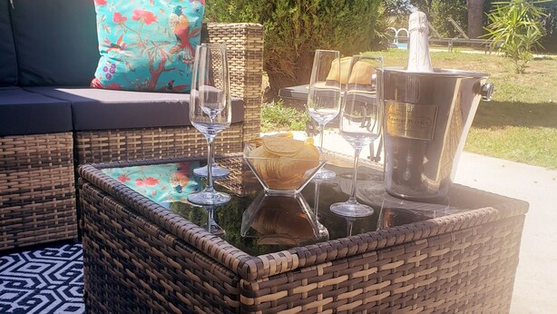 Un área de estar al aire libre con muebles de mimbre, una mesa con cubierta de vidrio, copas de vino y una botella de champán.