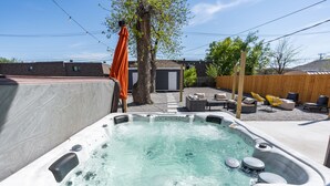 Ein Whirlpool in einem Garten mit Holzzaun, Gartenmöbeln und einem Baum.