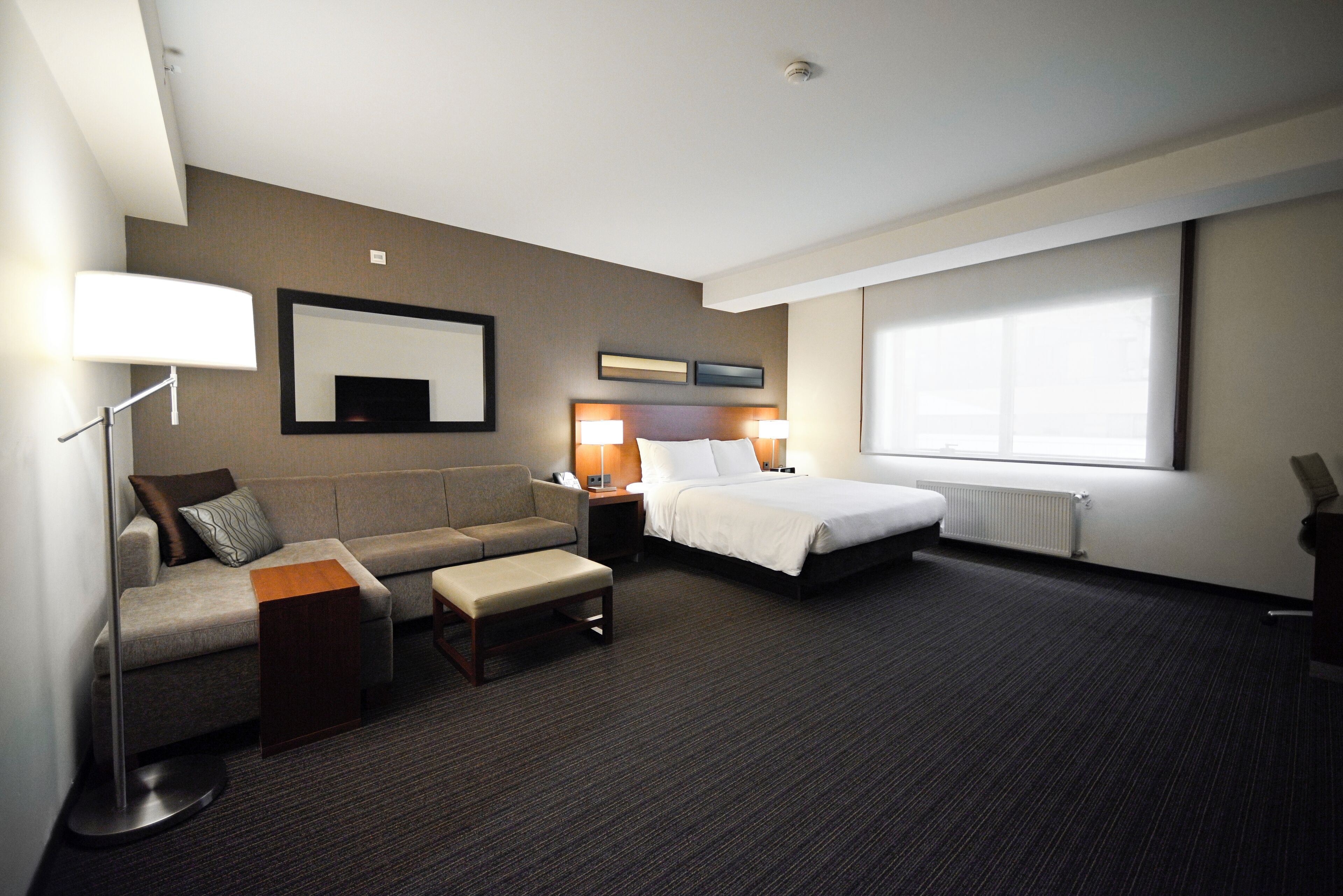Una habitación de hotel con cama, sofá, escritorio y un ventanal grande.