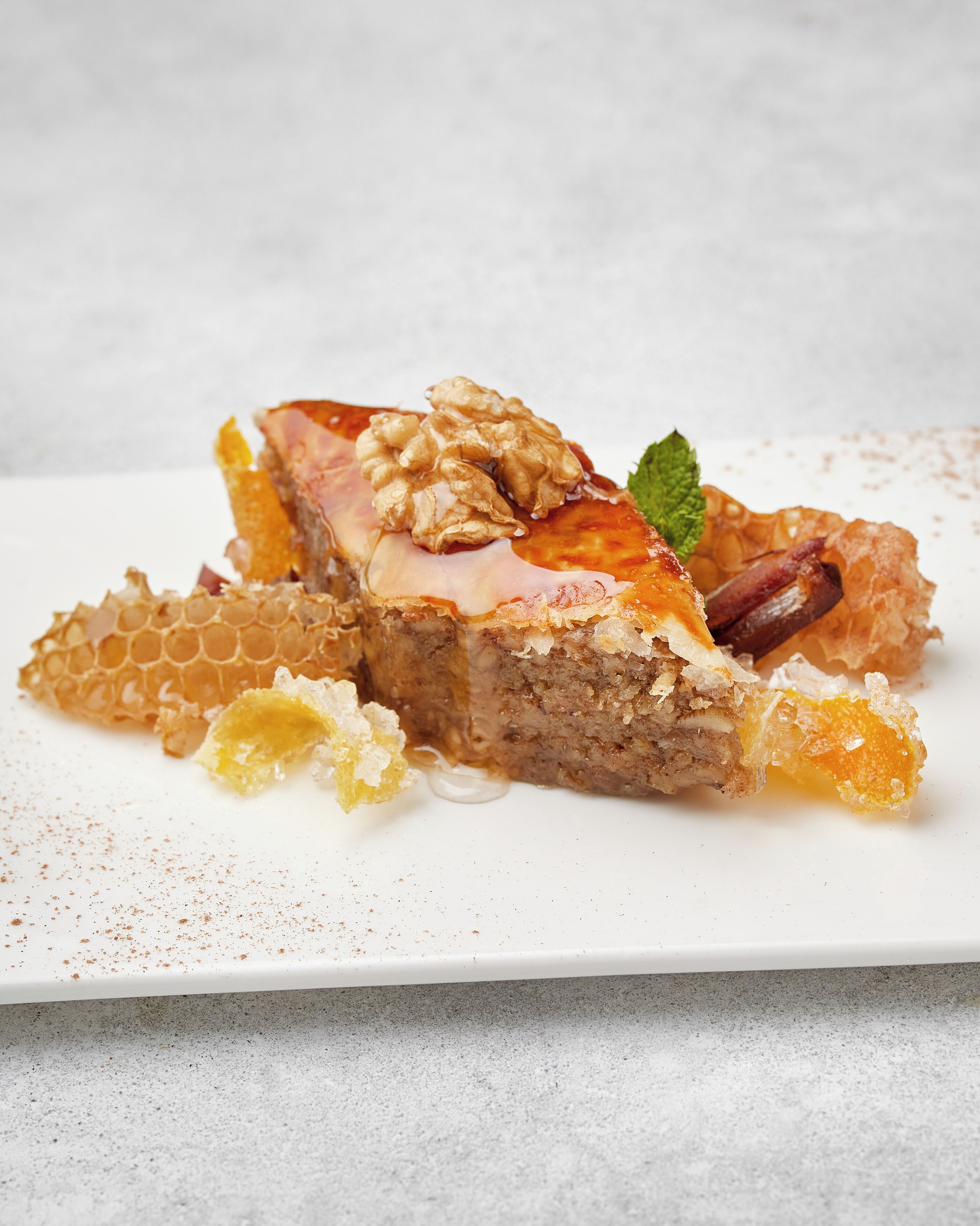 A dessert with honeycomb, a walnut, and a mint leaf on a white plate.