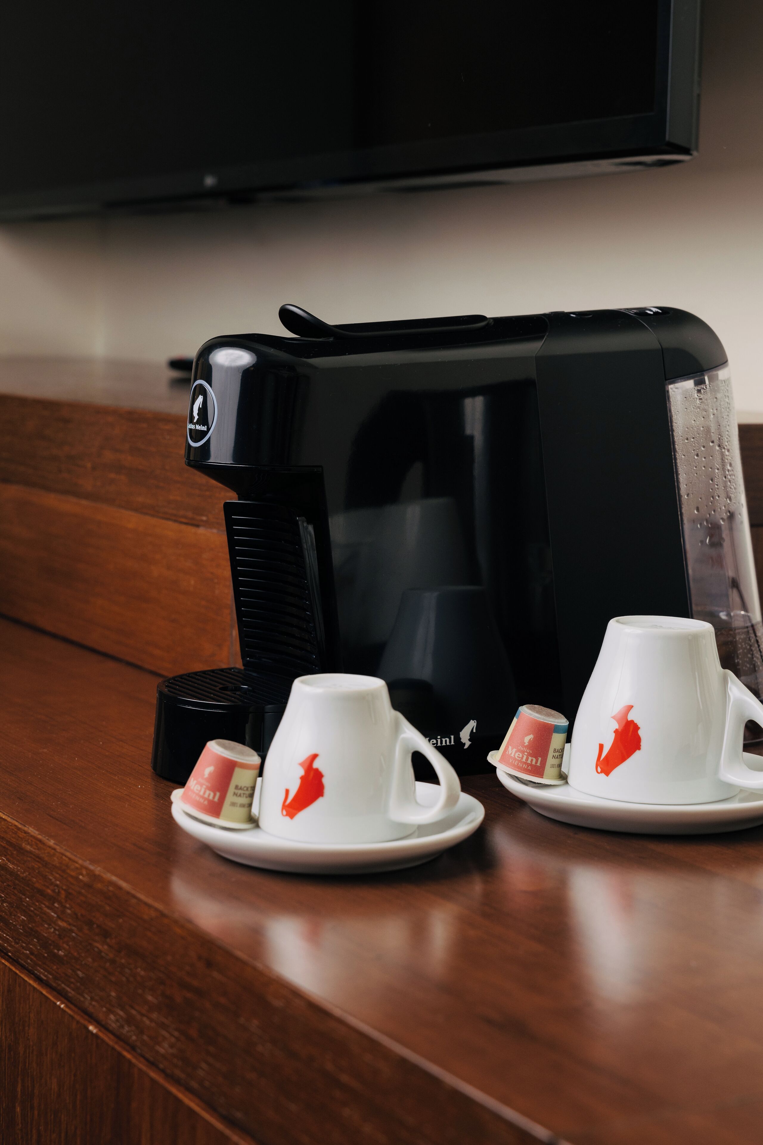 Eine Kaffeemaschine mit zwei weißen Tassen auf einem Holztisch.