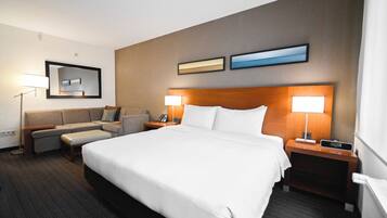 A hotel room with a large bed, two bedside tables with lamps, a sofa, a small table, and a wall-mounted mirror.