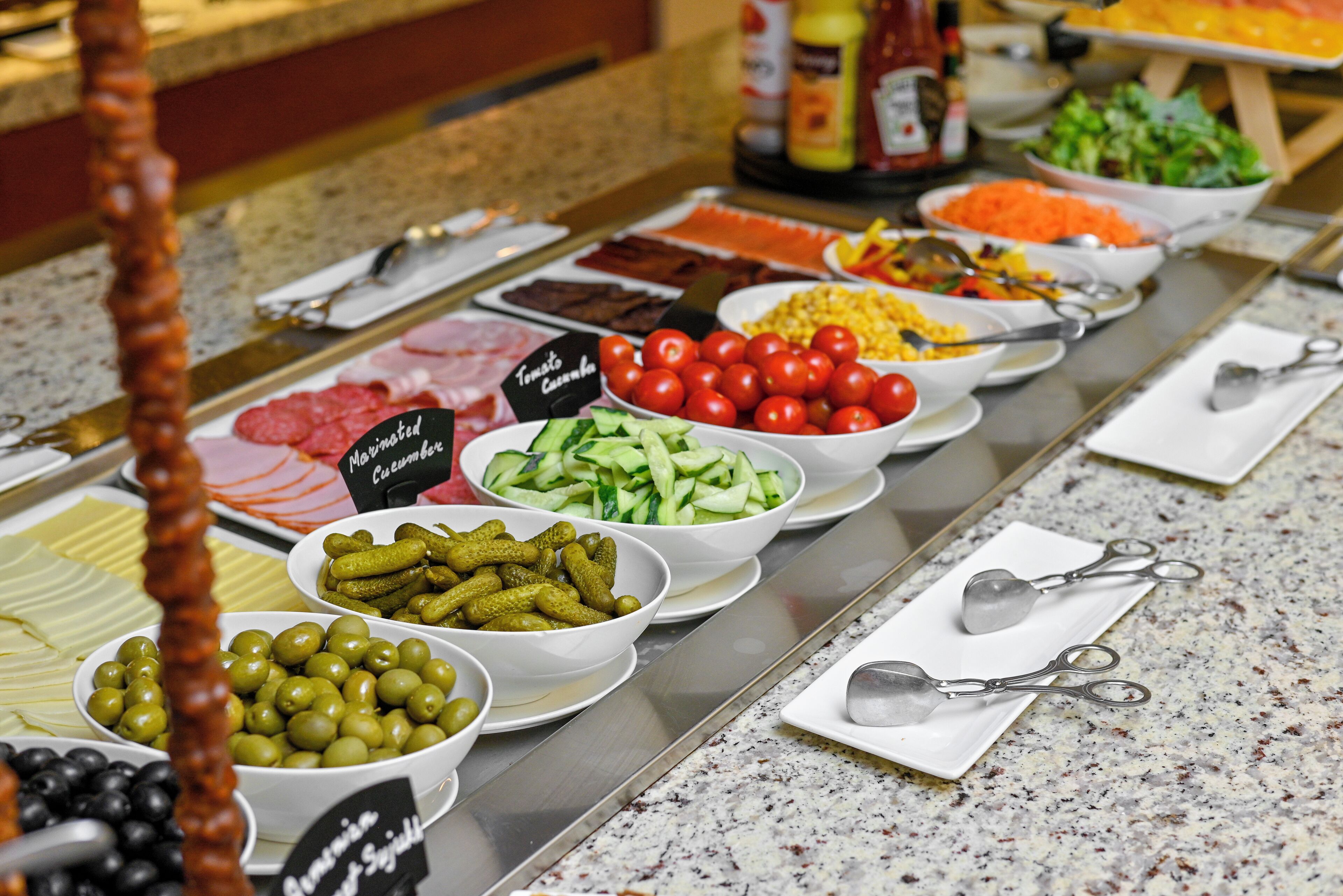 A buffet with various food items including meats, cheeses, olives, cucumbers, and tomatoes.