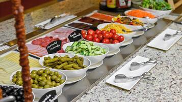 A buffet with various food items including meats, cheeses, olives, cucumbers, and tomatoes.