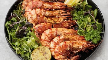 Eine Schüssel mit gegrillten Garnelen, Grünzeug und einer Limettenscheibe.