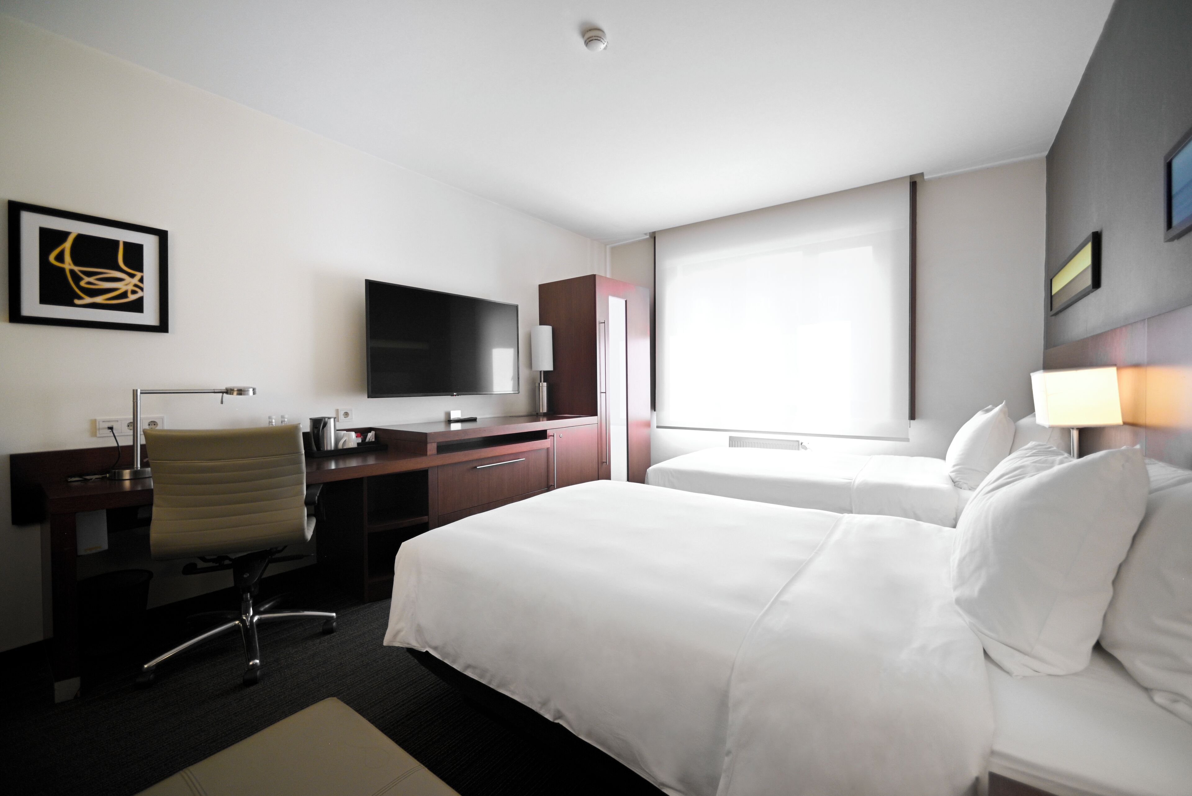 Een hotelkamer met een bed, een bureau, een stoel, een televisie en een raam.
