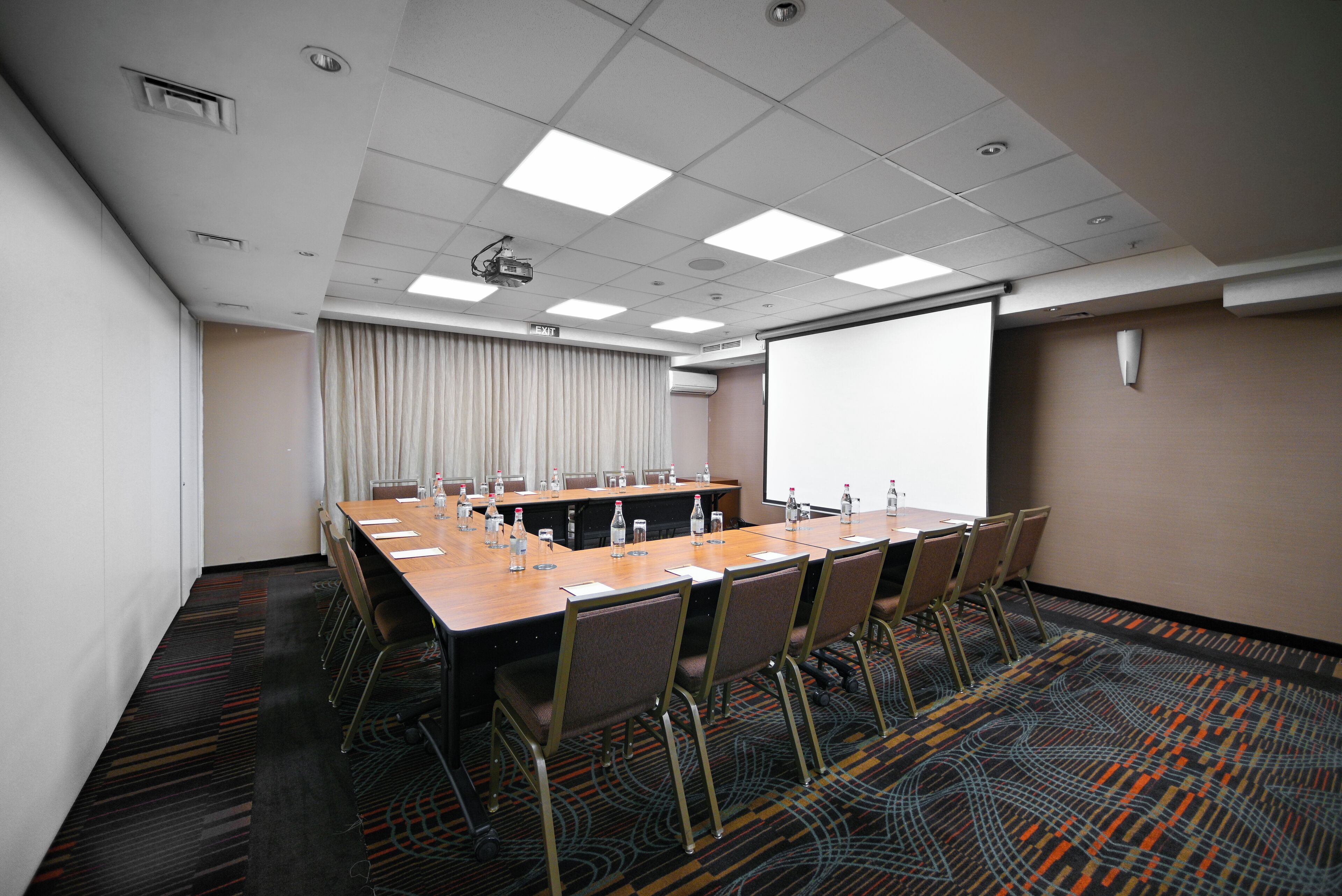 Una sala de conferencias con una larga mesa, sillas, un proyector y una pantalla.