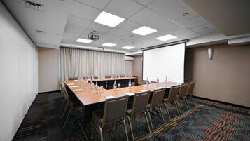 Una sala de conferencias con una larga mesa, sillas, un proyector y una pantalla.