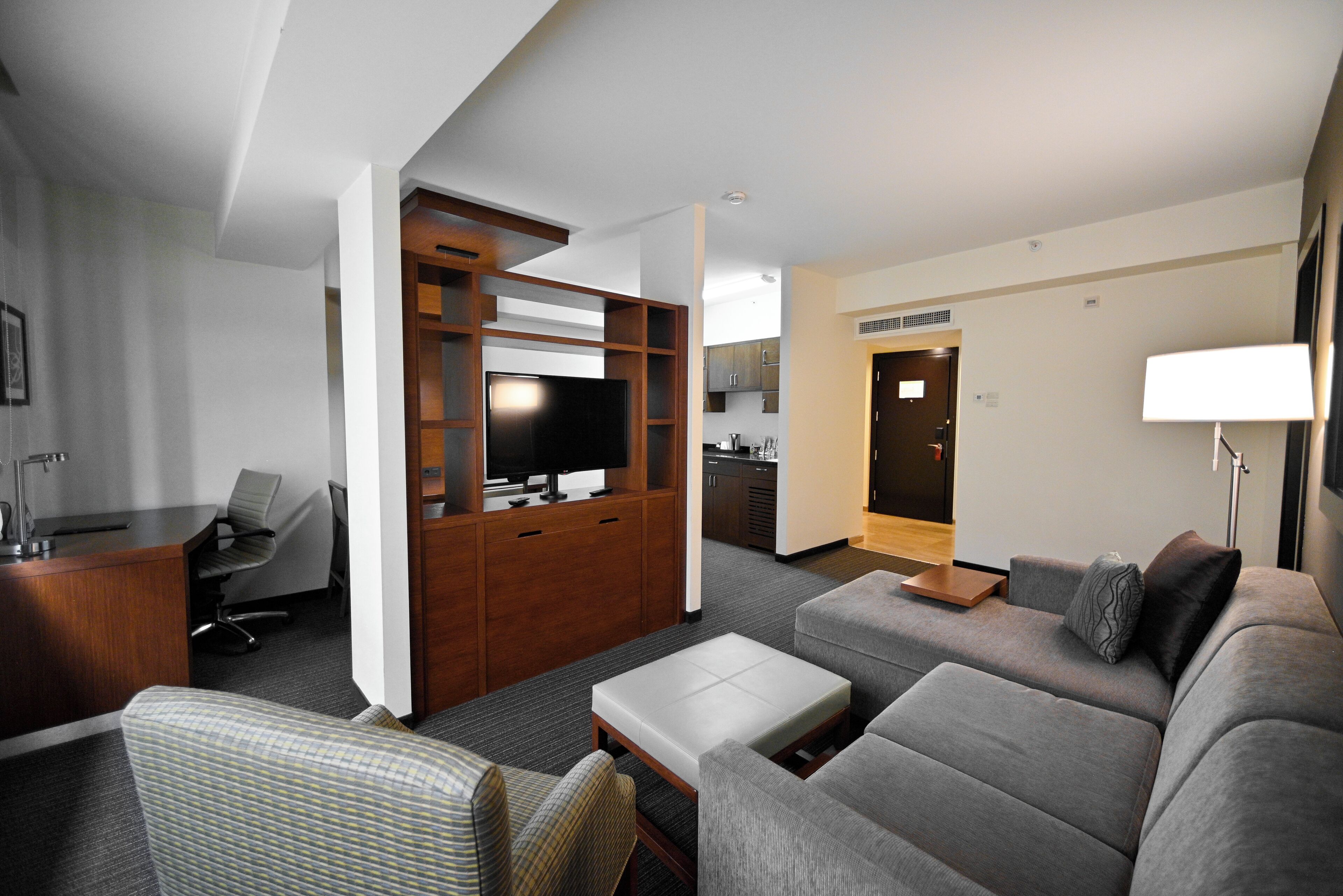 A hotel room with a sofa, a desk, a TV, and a kitchenette.