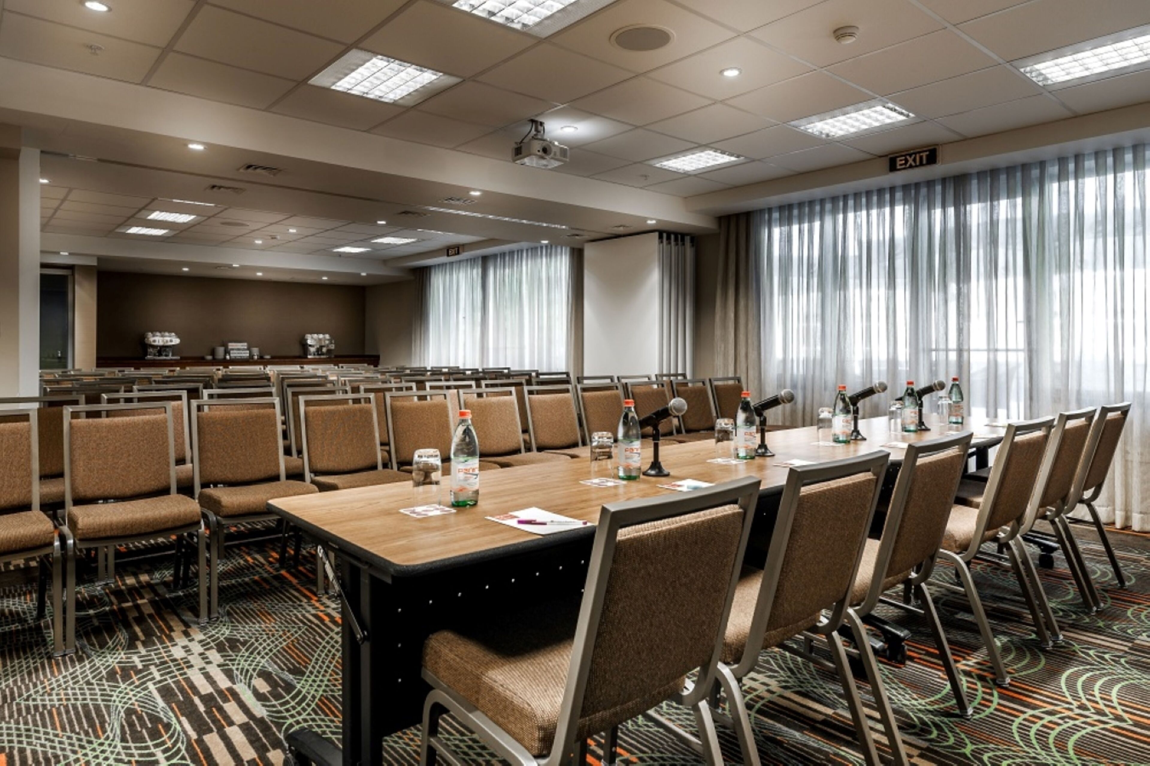 Une salle de conférence équipée de plusieurs tables, de chaises, d’un pupitre et d’un écran de projection.