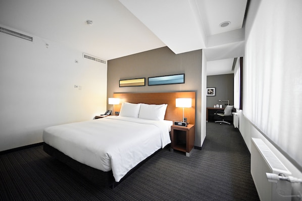 A hotel room with a large bed, bedside tables with lamps, a desk, and a chair. - Yerevan Place Hotel (Yerevan)