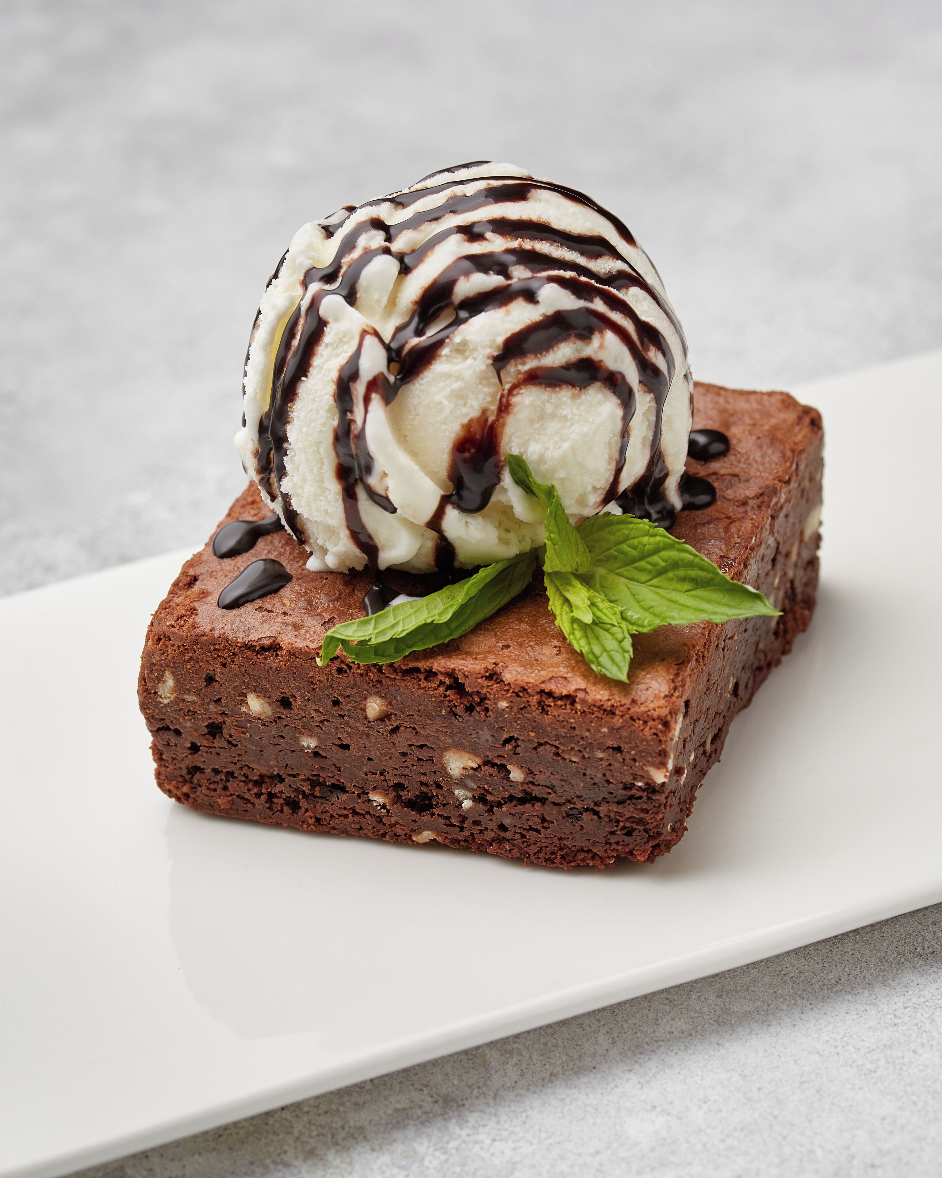 A dessert with chocolate brownie, ice cream, and chocolate drizzle on a white plate.