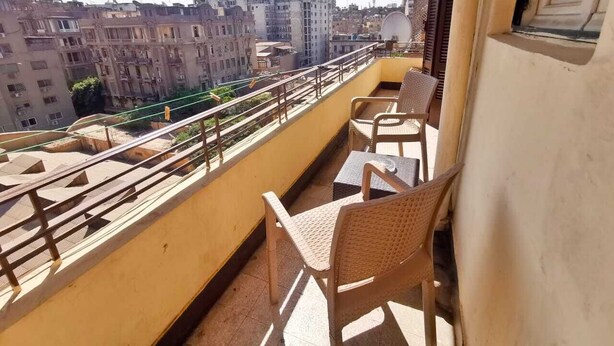 Uma varanda com cadeiras de vime e uma mesa, com vista para uma paisagem urbana com vários edifícios.
