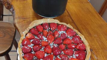 A wooden table with a pie topped with strawberries and powdered sugar, and a potted aloe vera plant.