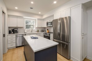 Una cocina moderna con armarios blancos, electrodomésticos de acero inoxidable y una isla central.