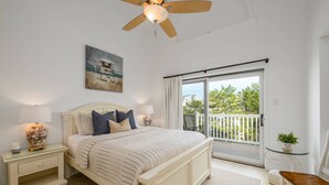 A bedroom with a bed, nightstands, a ceiling fan, a painting, a balcony with a view, and a small table with a plant. - 3rd House from the Beach, Water View, Comm. Pool (Fenwick Island)