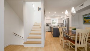 A modern kitchen with wooden flooring, a dining area with a table and chairs, and a staircase leading to another level. - 3rd House from the Beach, Water View, Comm. Pool (Fenwick Island)