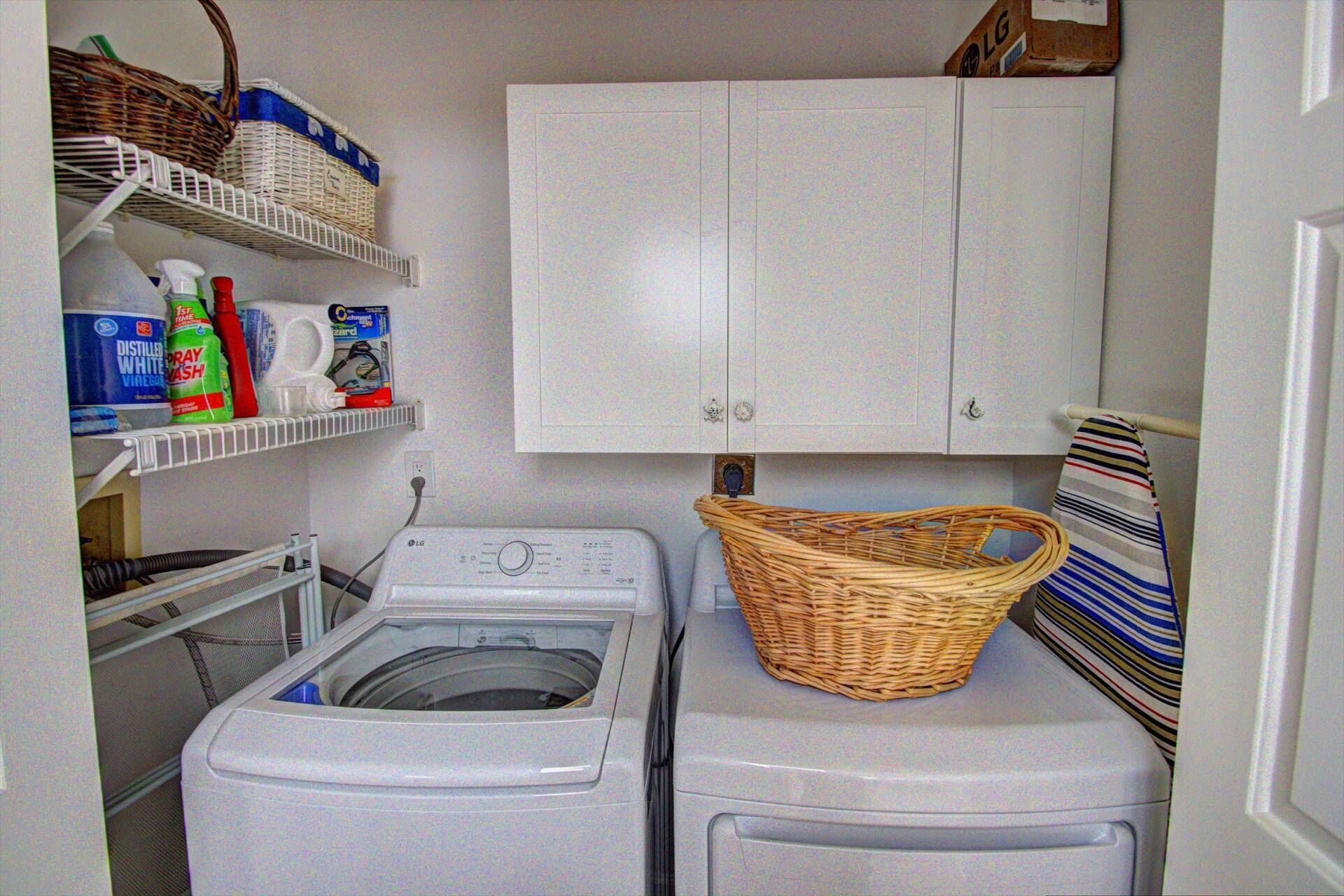A laundry room with a washing machine, dryer, shelves with cleaning supplies, and a wicker basket on the dryer.