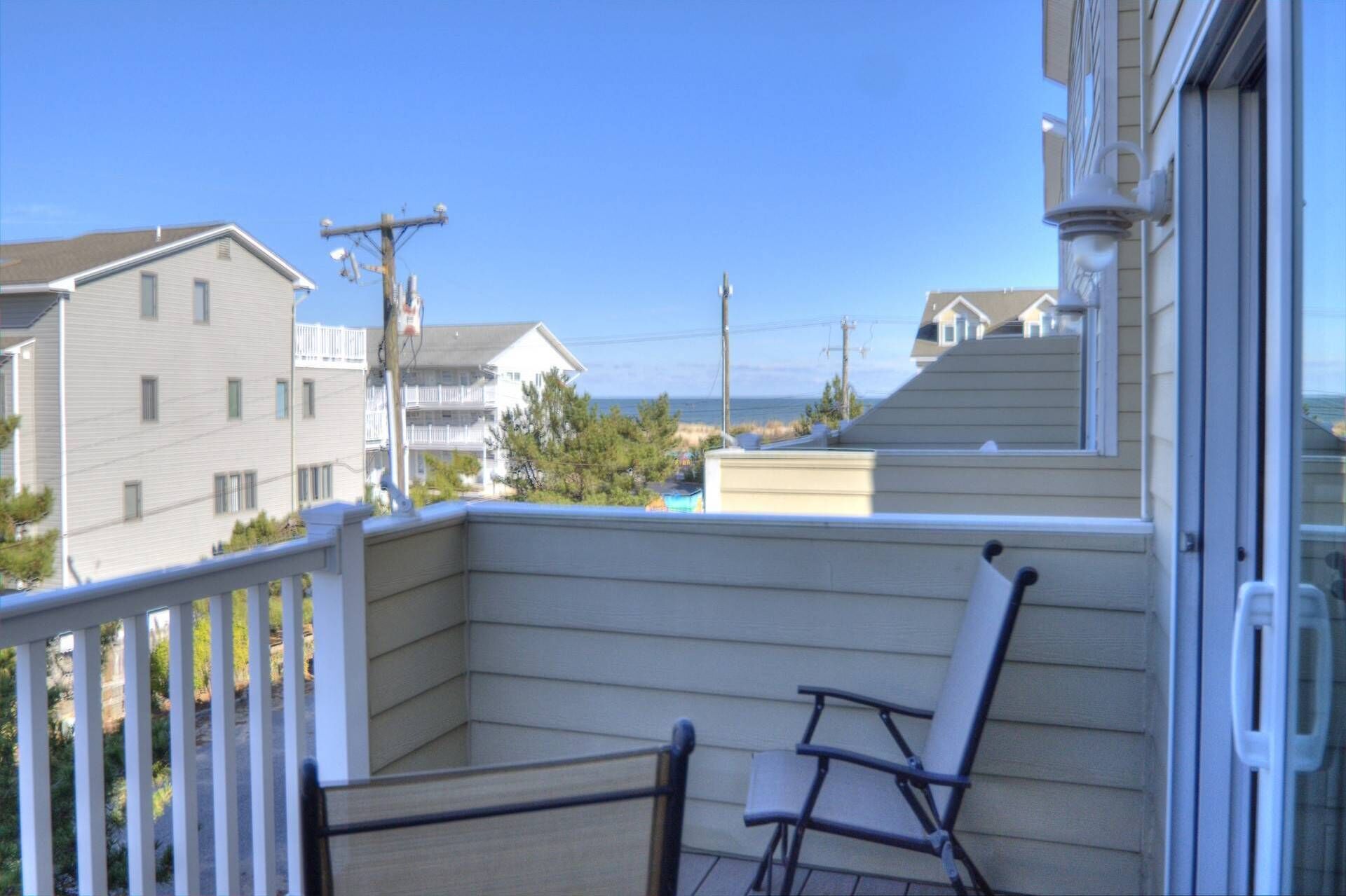 A balcony with two chairs, overlooking a residential area with houses and a clear sky.