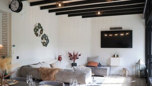 Un salon moderne avec un canapé gris, un téléviseur à écran plat et un coin repas avec une table dressée pour quatre personnes.